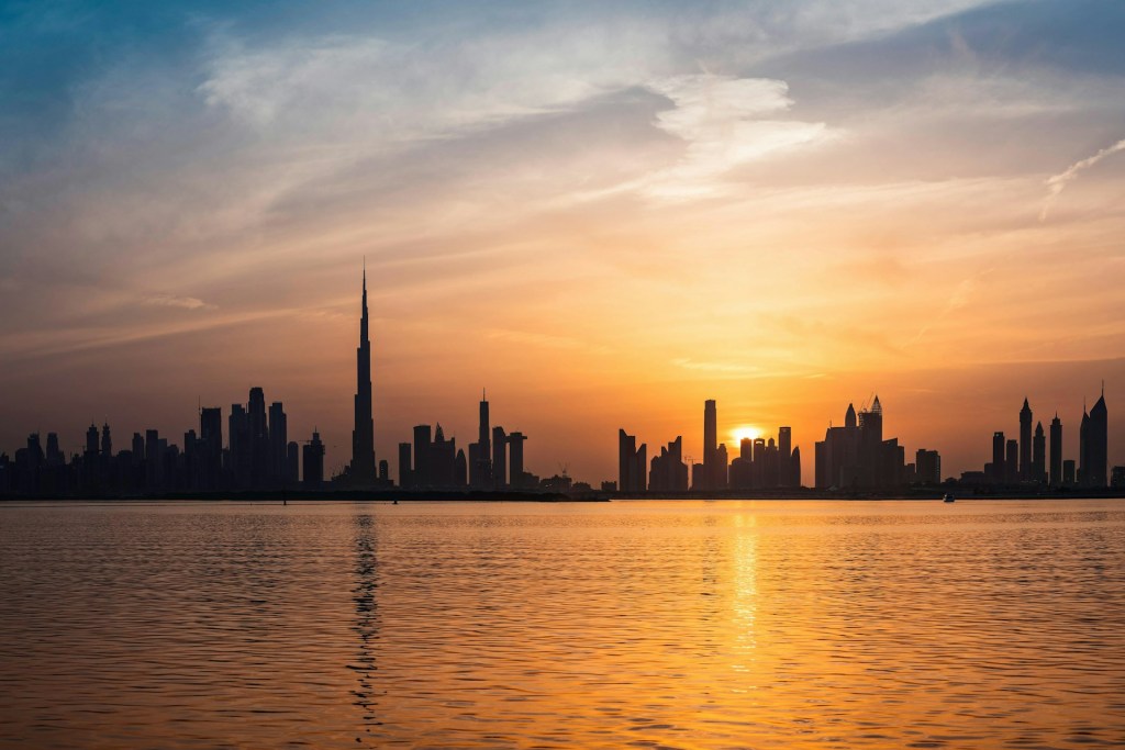 Dubai skyline at sunset featuring the Burj Khalifa, viewed across calm water, a serene moment